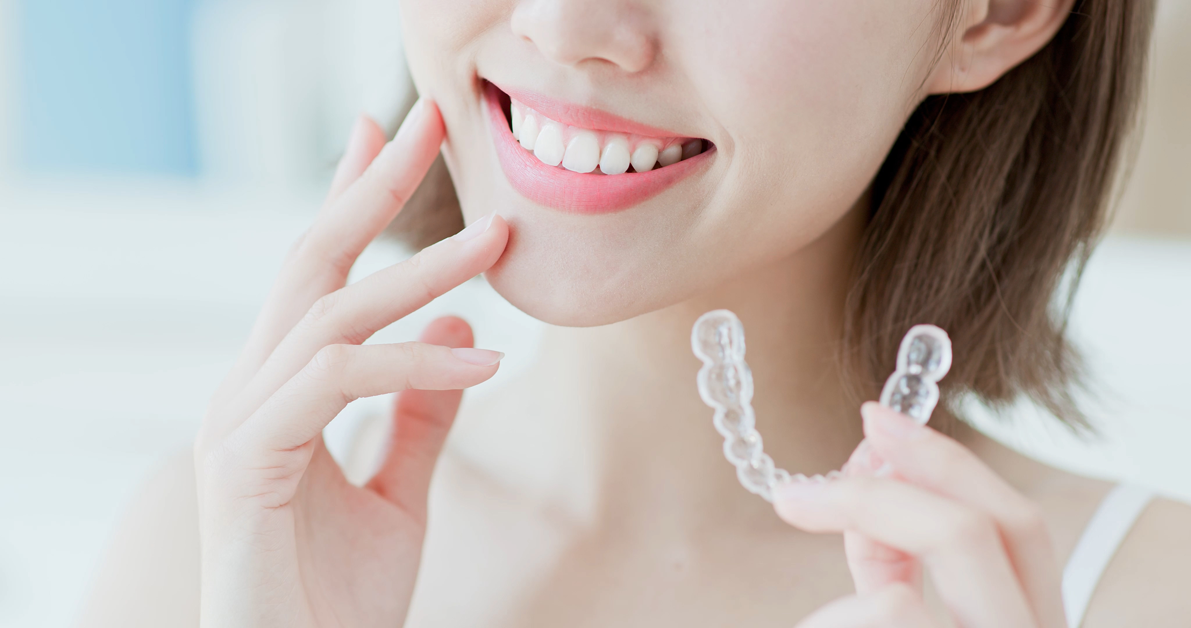 A woman's mouth smiling hold a clear aligner in her hand